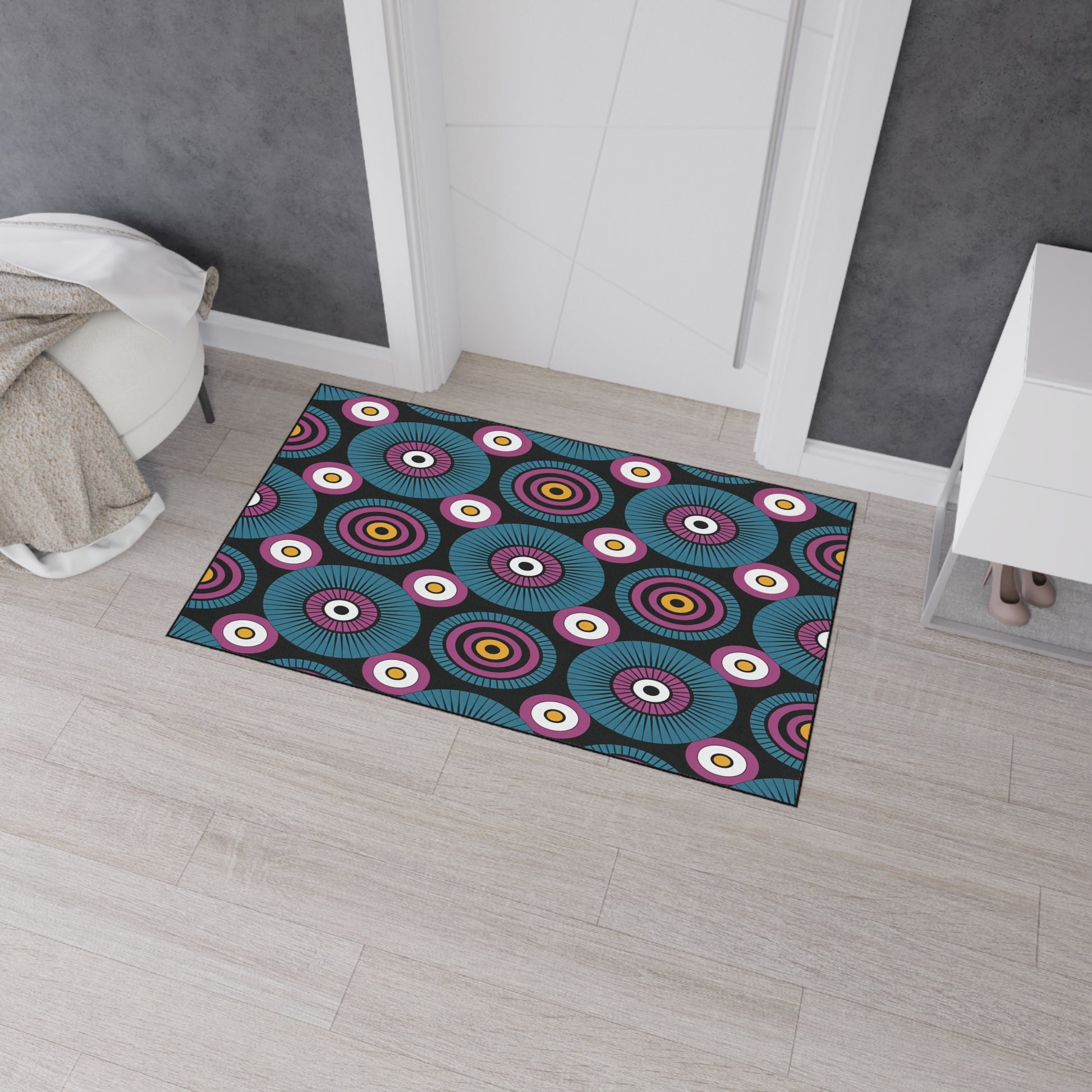 A rectangular doormat with a bold, colorful pattern of concentric circles in blue, purple, red, yellow, and white brings African-inspired aesthetics to a light wood floor. This custom floor mat features non-slip rubber backing for added safety.