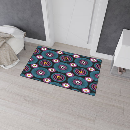 A rectangular doormat with a bold, colorful pattern of concentric circles in blue, purple, red, yellow, and white brings African-inspired aesthetics to a light wood floor. This custom floor mat features non-slip rubber backing for added safety.