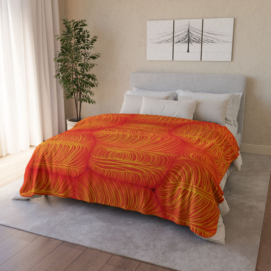 A neatly made bed with a gray upholstered headboard has white pillows and an African-inspired fleece blanket with vibrant orange and yellow patterns. The bed sits on a light gray rug, bringing cozy home decor style to this space. A potted plant is beside the bed.