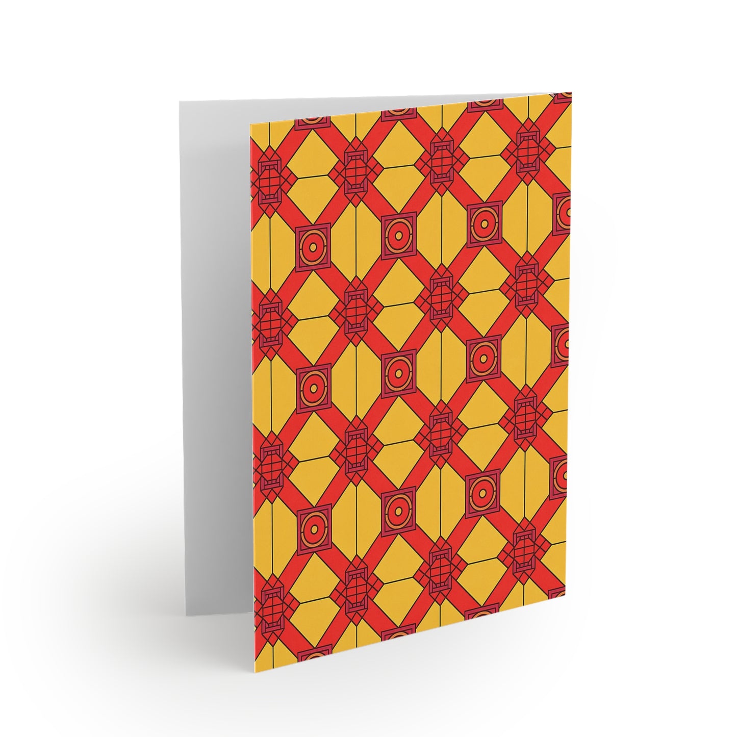 A greeting card standing upright features a geometric pattern of yellow and orange shapes with red outlines and accents, forming diamond and square motifs across the front—reminiscent of African-inspired greeting cards. The inside is blank and visible along the left edge.