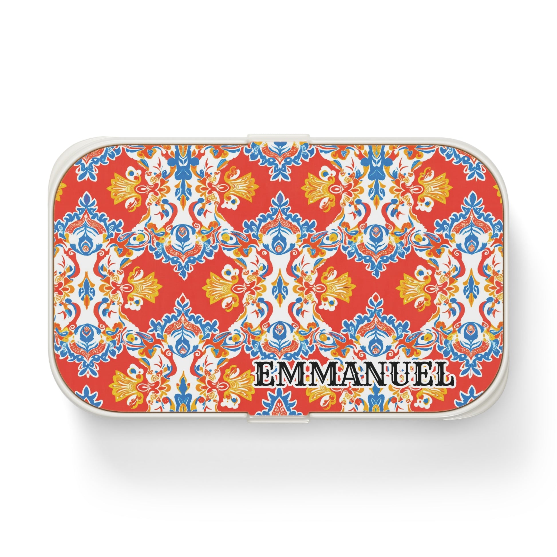 A rectangular, African-inspired bento lunch box with vibrant red, yellow, blue, and white ornamental floral patterns. “EMMANUEL” is boldly printed on the lower right of the lid, and the personalized lunch box features rounded white edges.