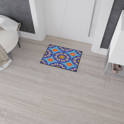 A small, rectangular mat with a vibrant geometric mandala pattern in blue, yellow, orange, and purple lies on light wood flooring near a white door. Its non-slip rubber backing keeps it secure next to a white dresser holding beige heels and a white chair.