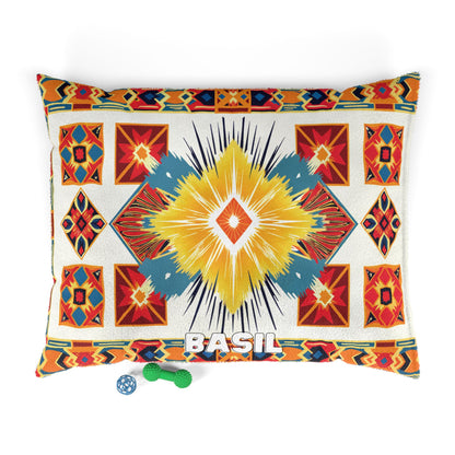 A rectangular pillow with a vibrant, African-inspired geometric pattern in red, yellow, turquoise, and orange. BASIL is written in white at the bottom center. Two small dog toys—a green bone and a blue ball—sit beside the pillow on a white background.