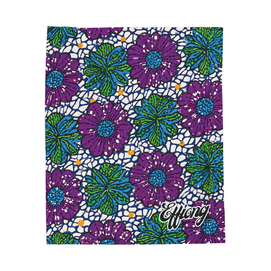 A vibrant, African-inspired blanket features bold purple flowers with blue centers and green leaves on a white background with blue and orange dots. The word Effiong appears in white script at the bottom right corner—a stunning custom gift.