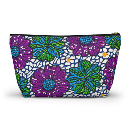 A zippered T-bottom pouch featuring a bold, colorful floral pattern with large purple and green flowers, blue leaves, scattered yellow dots, and a black mosaic-like overlay draws inspiration from African-inspired patterns. Black zipper with gold pull tab.