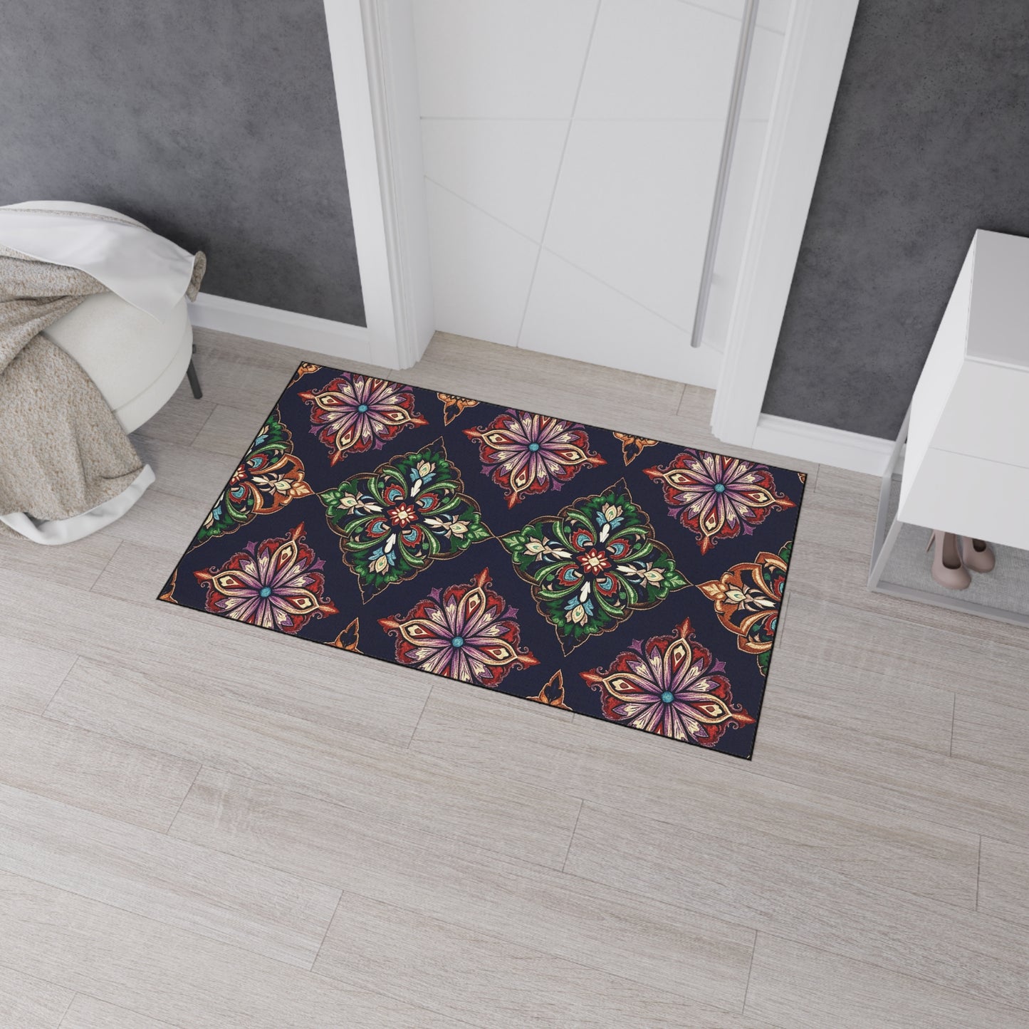 A colorful doormat with an ornate, symmetrical floral pattern in red, green, gold, and purple—a great pick for African-inspired home decor—sits on a light wood floor by a white door. It features non-slip rubber backing for added safety.