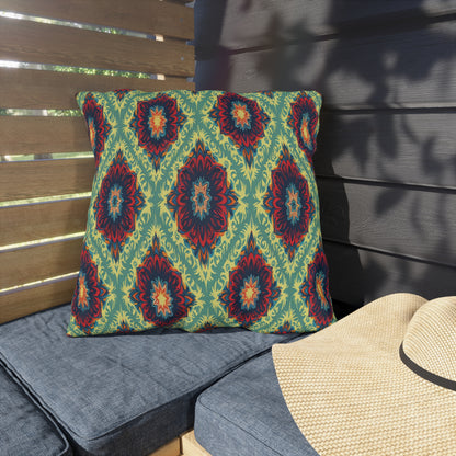 A square cushion with an African-inspired geometric and floral pattern in green, blue, orange, and red rests on a gray outdoor bench. Beside it is a straw hat. Wooden slats and dark siding create a shaded, cozy patio setting.