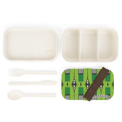 An African-inspired lunch box set featuring a green patterned lid, brown elastic strap, fork, spoon, and a two-part white container with three compartments is neatly arranged on a white background.
