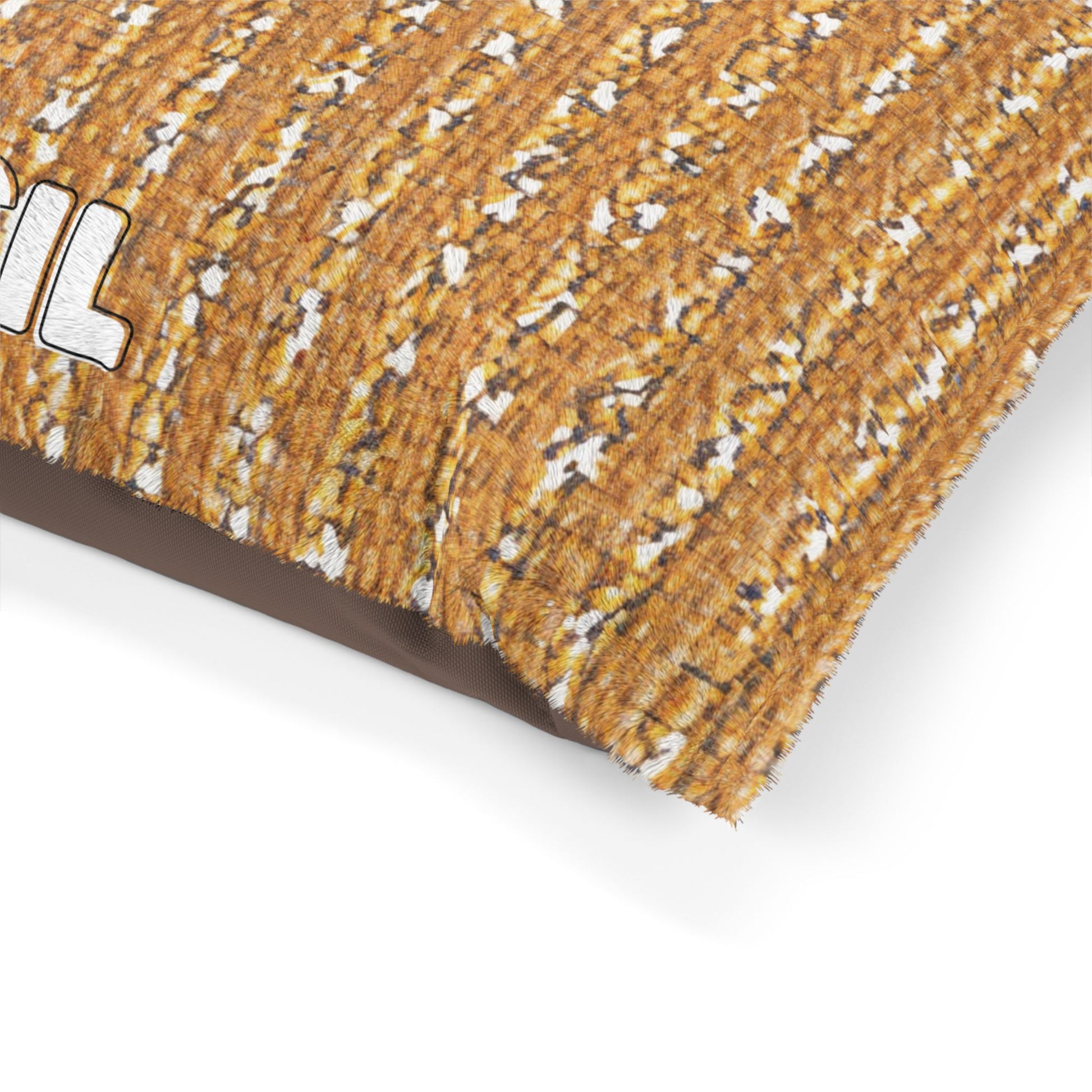A close-up of a rectangular custom pet pillow with a textured, brown and tan woven pattern resembling a field of wheat. The partial letters IL in bold white font with a black outline are visible on the left side, set against a white background.