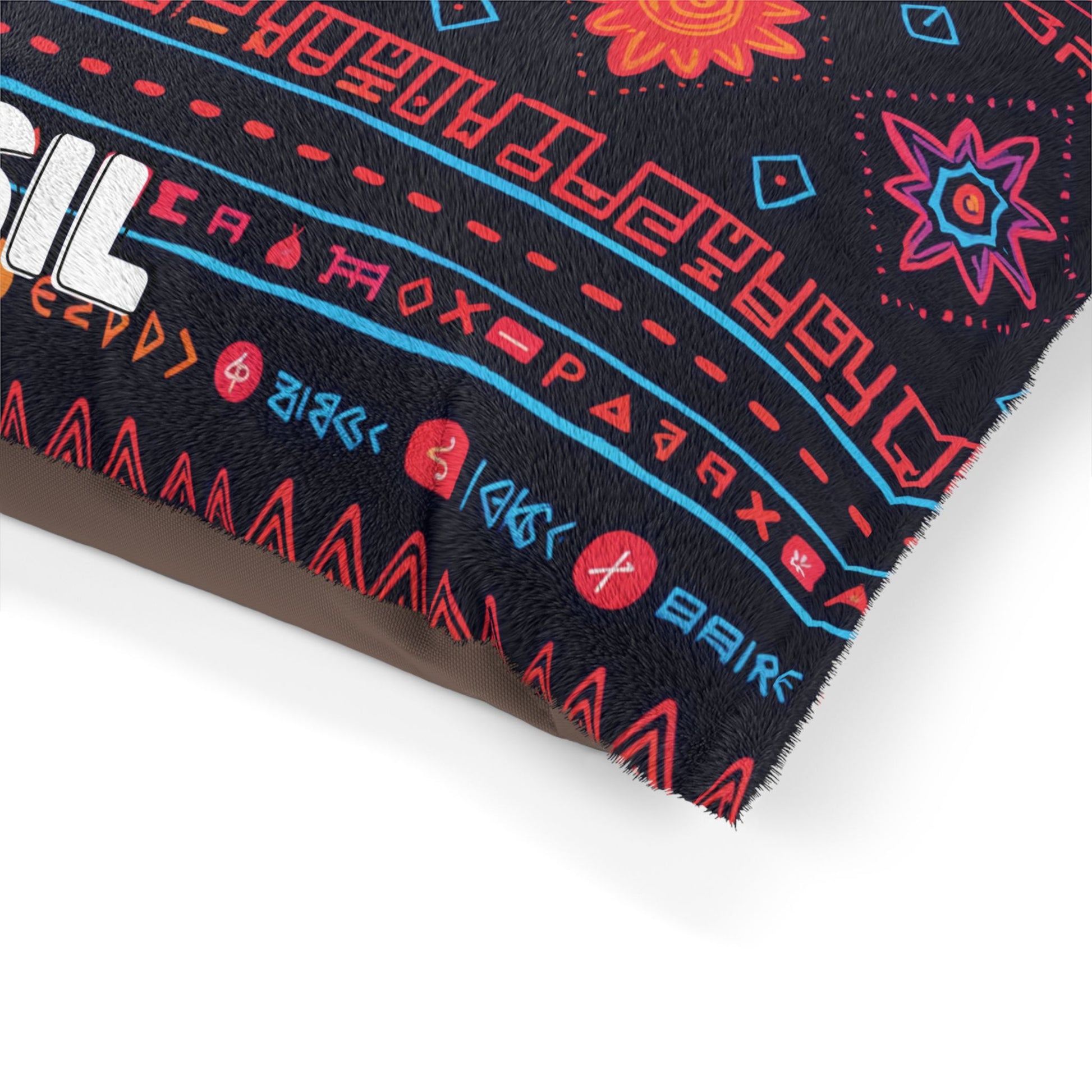 A close-up of a pillow corner with an African-inspired geometric and floral pattern in red, blue, and orange on a black background. Red circular symbols with white glyphs line the edge, and part of white block text appears on the left.