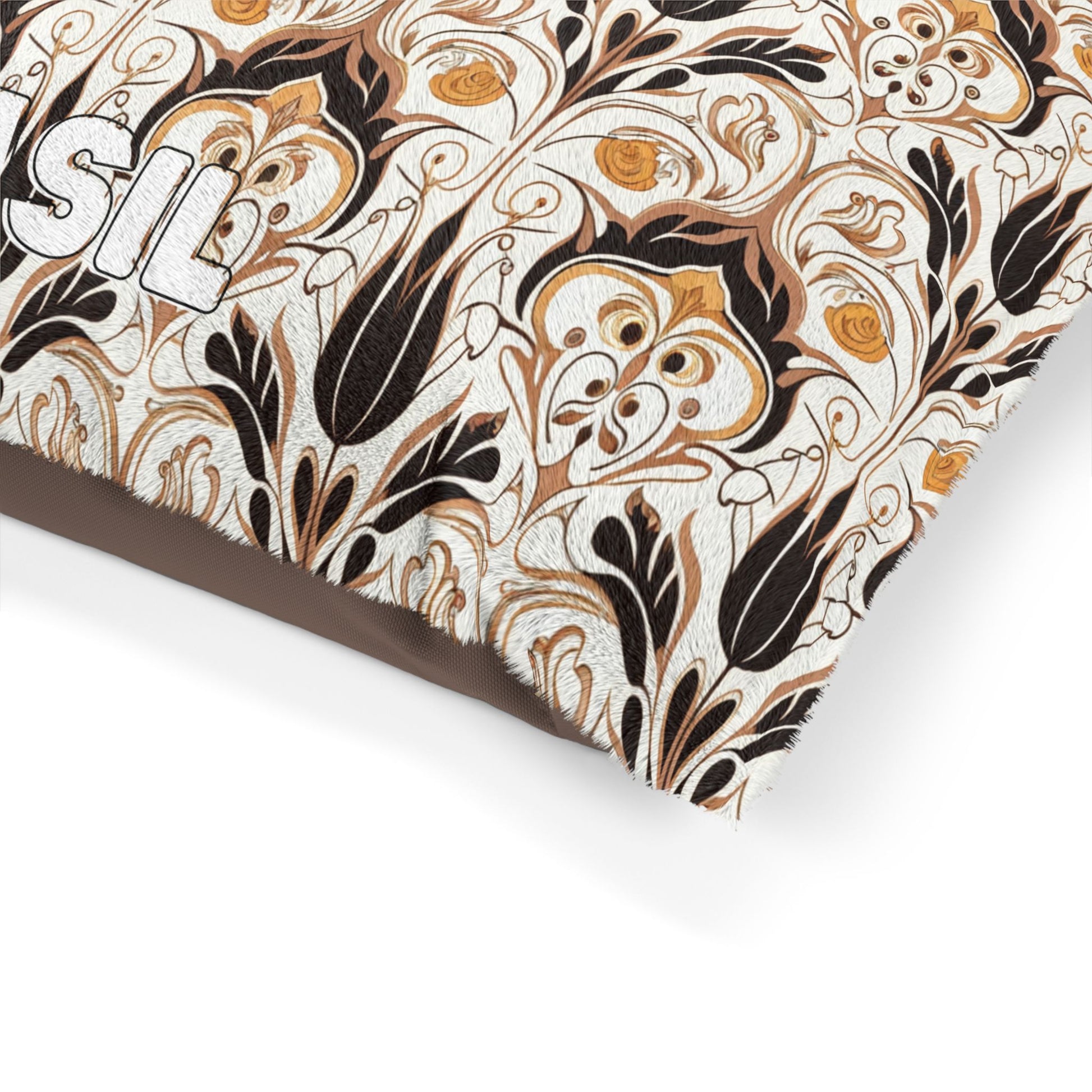 A close-up of a cushion with an African-inspired floral pattern in black, gold, and brown on a cream background. Part of a white embroidered word, “SIL,” is visible on the left edge. The fabric appears textured and the design is intricate and ornate.