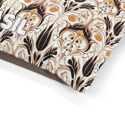 A close-up of a cushion with an African-inspired floral pattern in black, gold, and brown on a cream background. Part of a white embroidered word, “SIL,” is visible on the left edge. The fabric appears textured and the design is intricate and ornate.