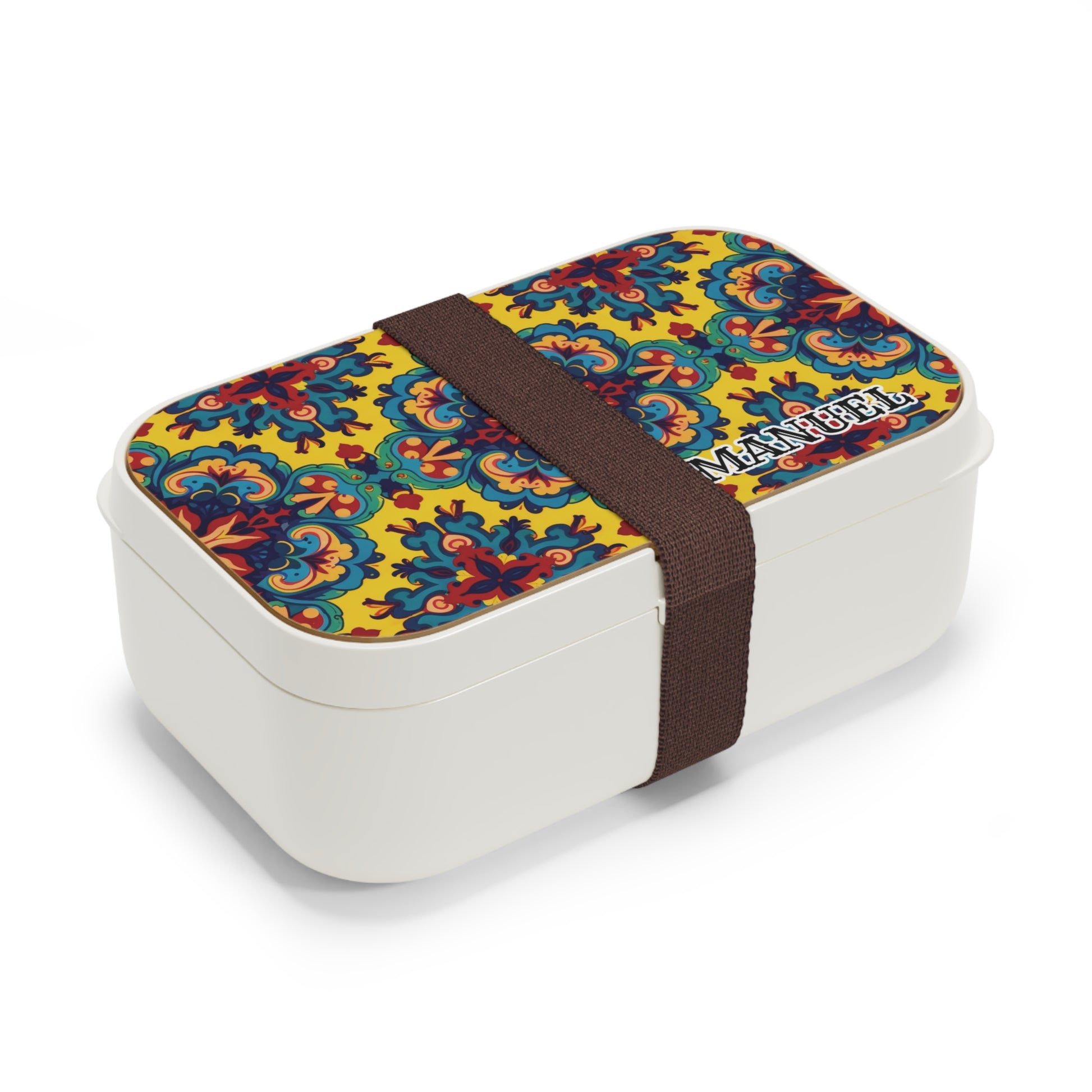 A white African-inspired bento lunch box with a colorful floral and geometric pattern on the lid, secured by a wide dark brown elastic band. The word MANOEL is printed on the BPA-free lunchbox in bold letters near one corner.