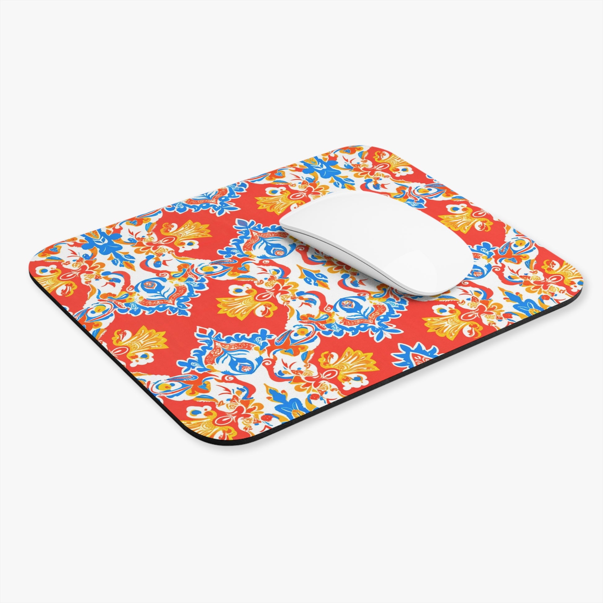 A white wireless computer mouse rests on an African-inspired mouse pad with a vibrant red background, colorful floral patterns, and a non-slip rubber base—an eye-catching, vibrant desk accessory for any workspace.
