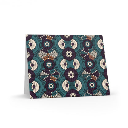 A standing card displays a geometric pattern of overlapping circles and star shapes in teal, cream, brown, and dark purple. The symmetrical design features intricate lines and repetitive motifs, reflecting culturally inspired designs and premium stationery.