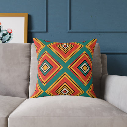 A vibrant throw pillow featuring a colorful geometric diamond pattern in red, yellow, orange, and green sits on a light gray couch. The background wall is dark blue, with a framed cactus print partially visible to the left.