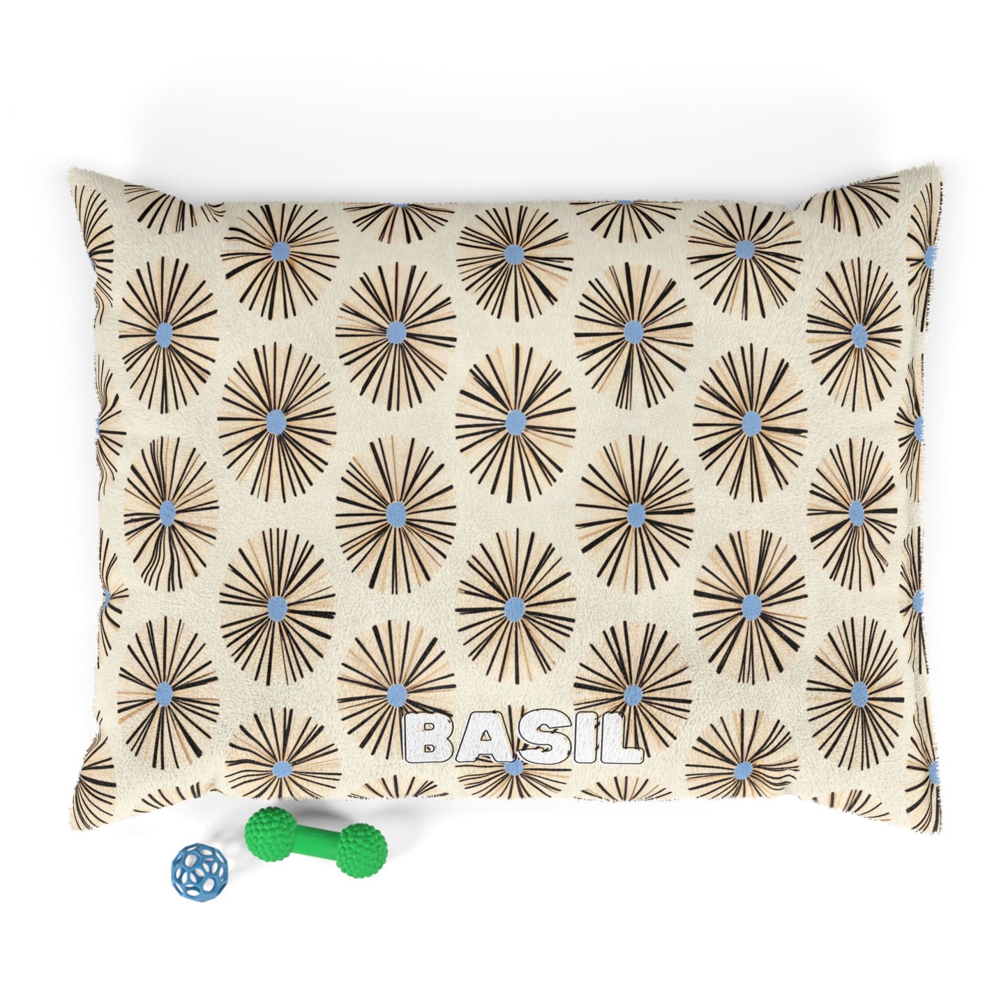 A cream-colored rectangular pillow with an African-inspired brown and blue geometric flower pattern and the name BASIL in white block letters. Two small green and blue dog toys sit near the bottom left corner on a white background.
