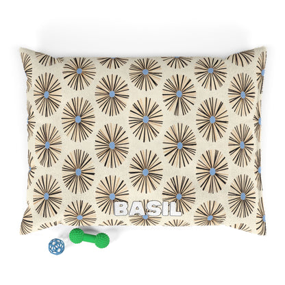 A cream-colored rectangular pillow with an African-inspired brown and blue geometric flower pattern and the name BASIL in white block letters. Two small green and blue dog toys sit near the bottom left corner on a white background.