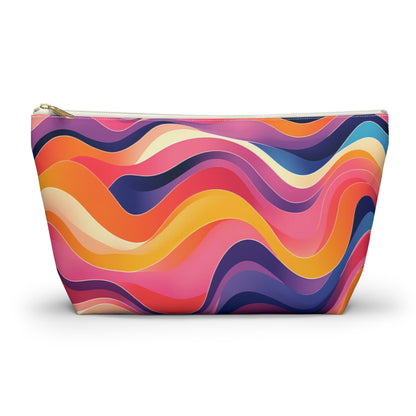 A vibrant cosmetic travel bag with a wavy, African-inspired pattern in pink, orange, yellow, purple, and dark blue. The contour-like lines create a lively abstract design. This T-bottom pouch stands upright with a gold zipper at the top.