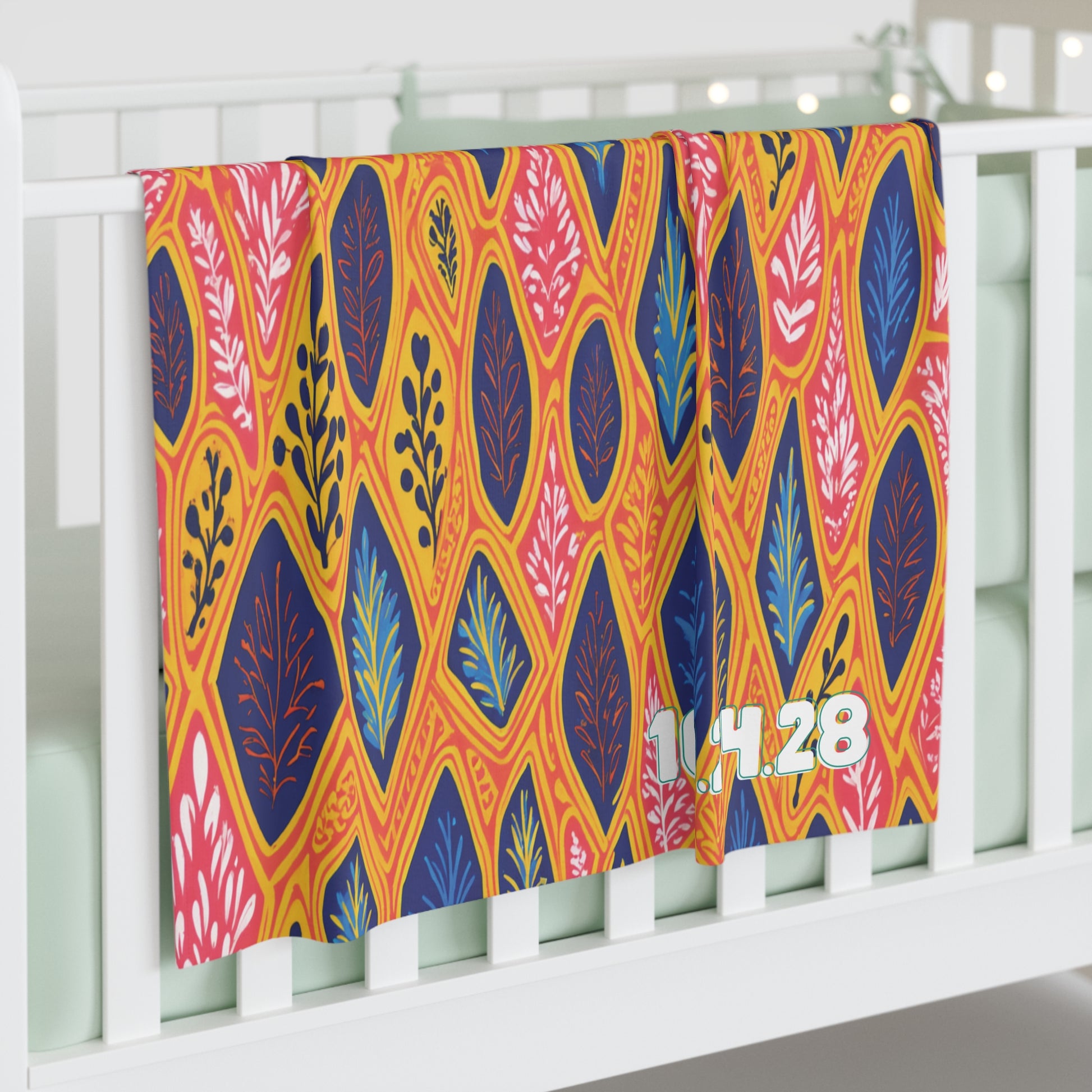 A colorful personalized baby blanket with an orange, yellow, pink, and blue leaf pattern hangs over the side of a white crib. The numbers 1.14.28 are printed in white and mint green. The crib bedding is mint green, adding to the cozy nursery look.