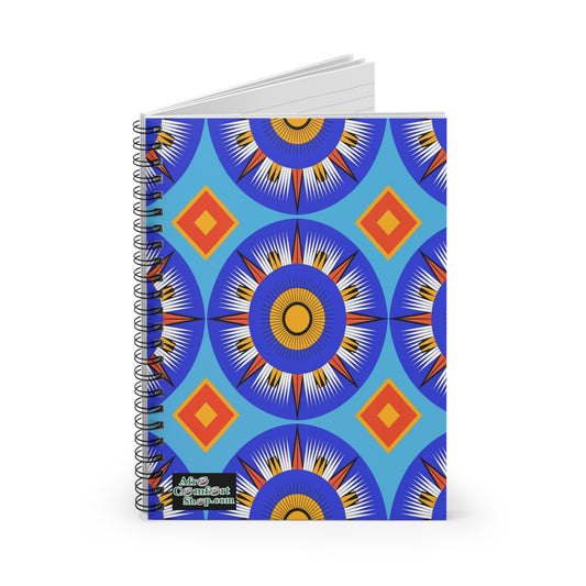 A spiral notebook with a vibrant cover featuring culturally inspired designs—bold blue, orange, yellow, and white starburst circles with red diamonds on blue. The lower left corner displays a small “Afro Conscient Shop.com” logo.