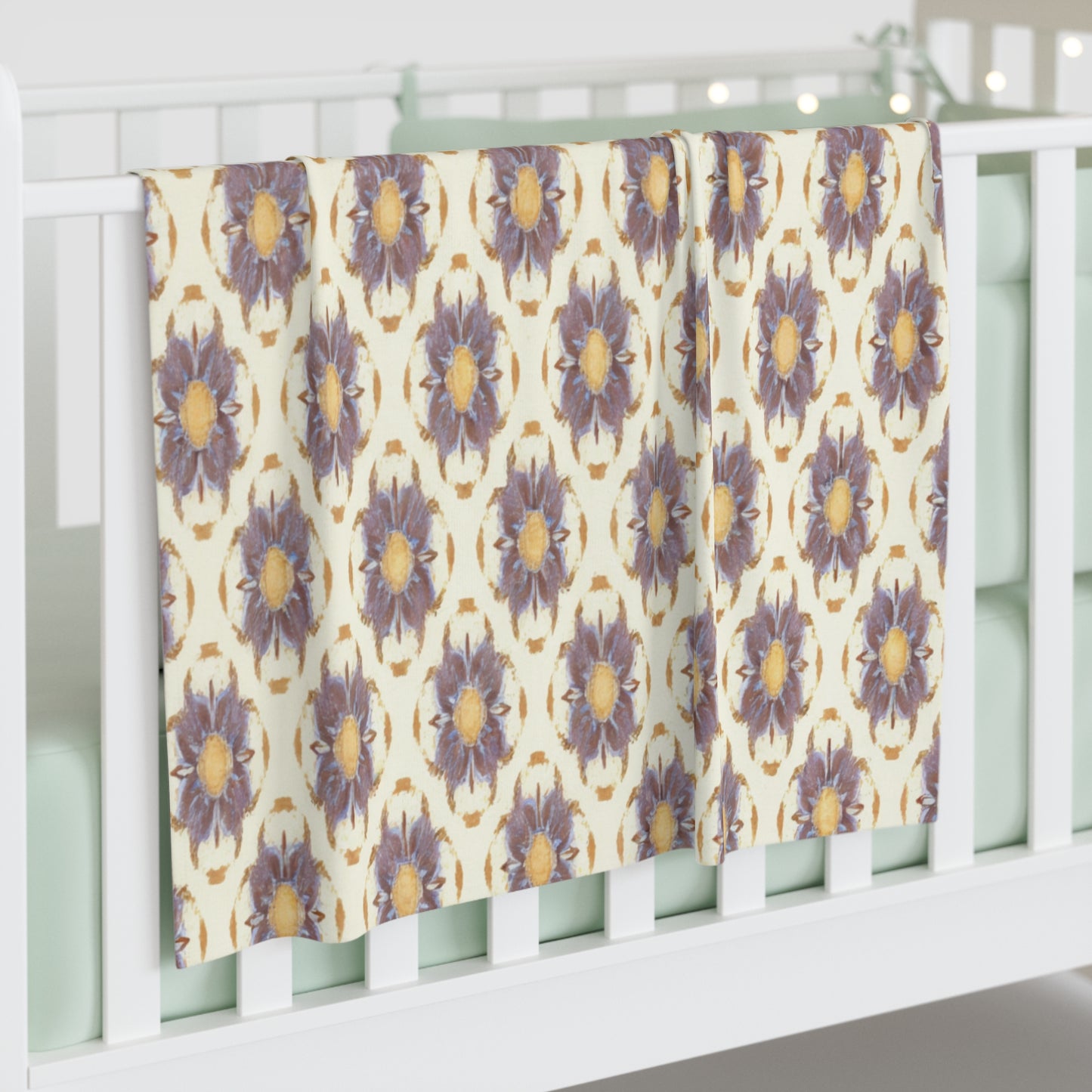 A white crib with mint green bedding has a personalized baby blanket draped over its rail. The blanket features a repeating pattern of large, purple and yellow flowers, adding a cozy and inviting touch to the nursery’s African-inspired decor.