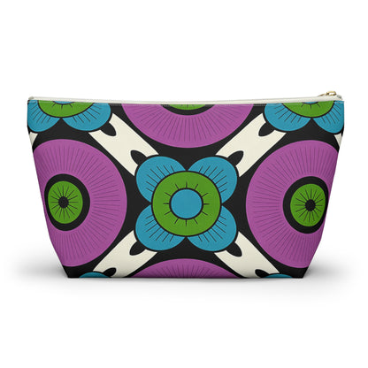A cosmetic travel bag with a bold, colorful geometric floral pattern inspired by African patterns. Large purple circles, blue flowers with green centers, and black-and-white accents create a modern, symmetrical T-bottom pouch on a cream background.