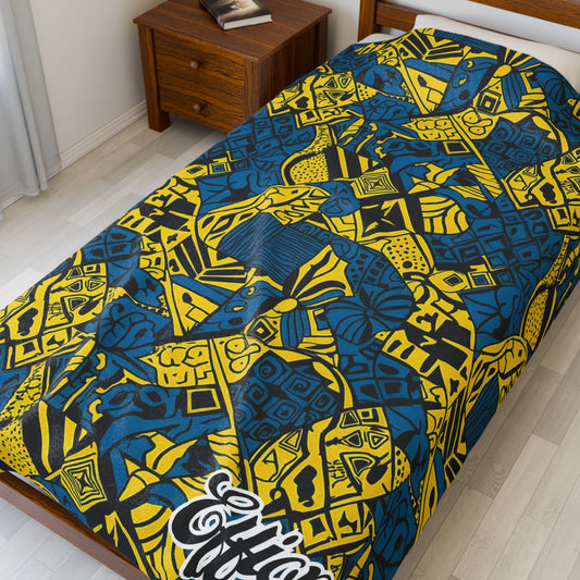 A twin bed with a vibrant blue and yellow African-inspired blanket featuring abstract geometric patterns and the word “Effort” in white script. A wooden nightstand beside the bed holds two closed books.