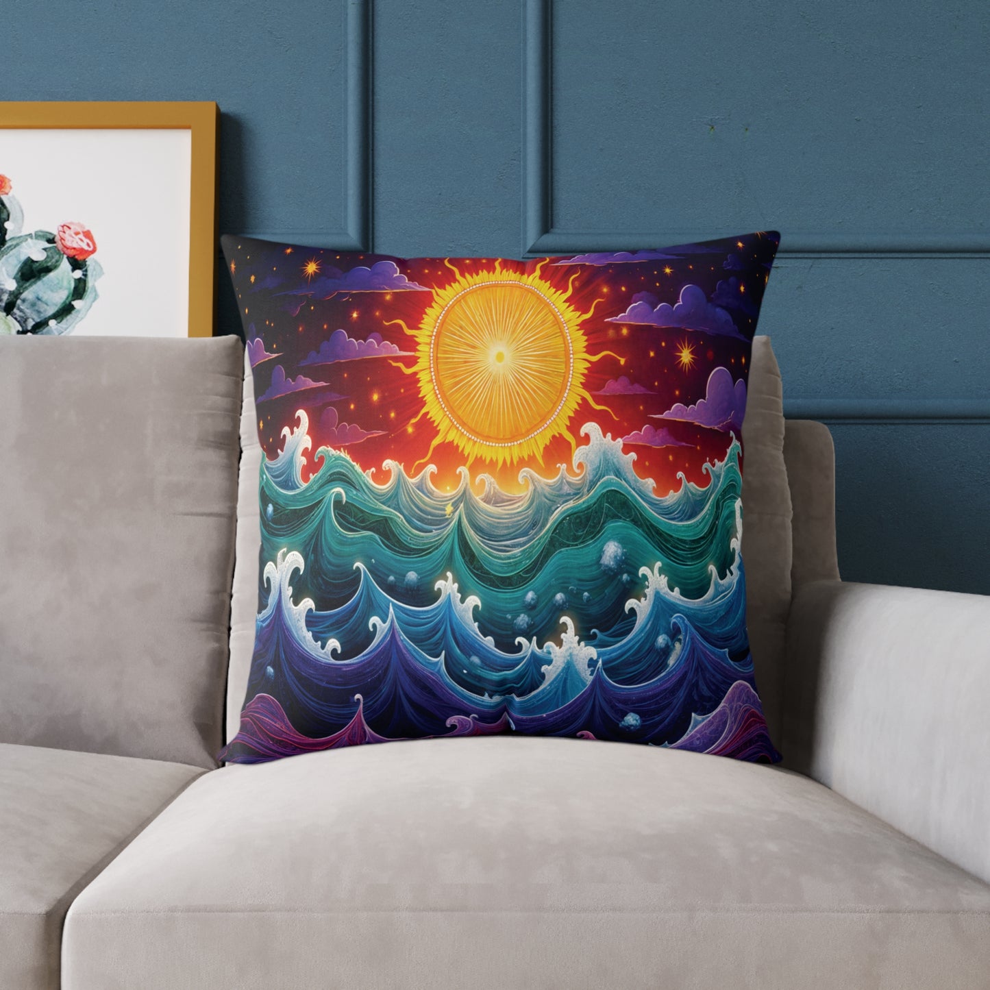 A vibrant throw pillow featuring golden sun art above multicolored ocean waves sits on a light gray couch against a blue wall. Part of a framed cactus illustration is visible, adding to the colorful home decor.