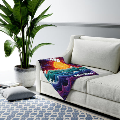 A bright, colorful personalized baby blanket featuring a sun and swirling ocean waves is draped over a modern white sofa. A large potted plant and hints of African-inspired decor complete the stylish, minimal room with a geometric rug and floor pillow.