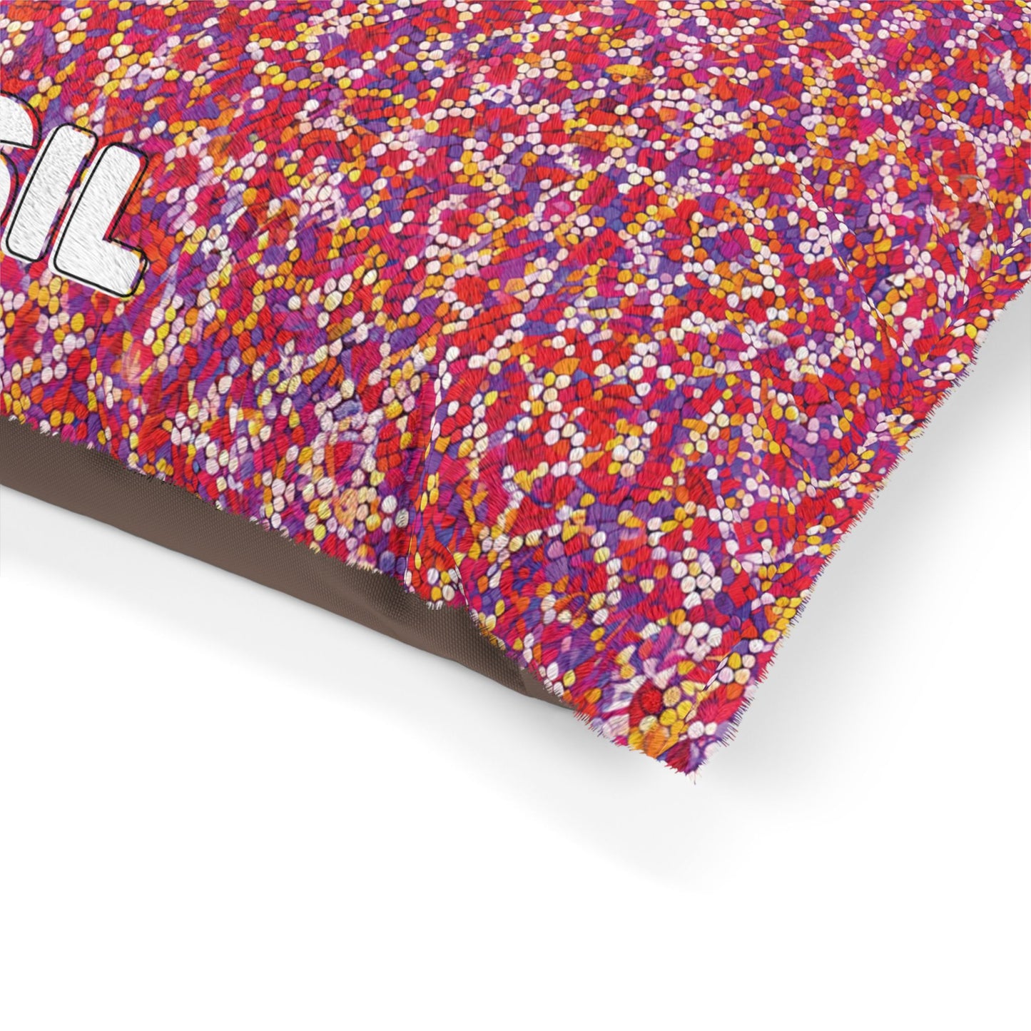A colorful pillow with durable construction features a dense pattern of tiny red, pink, orange, yellow, and white dots. Partial text SIL in bold white letters appears on the upper left. The pillow sits on a white background with a brown underside.