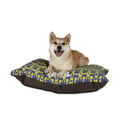 A happy Shiba Inu dog lies on a rectangular cushion with blue and yellow patterns and a solid dark brown base, enjoying luxurious comfort against a plain white background. The dog faces forward with its mouth open and tongue visible.
