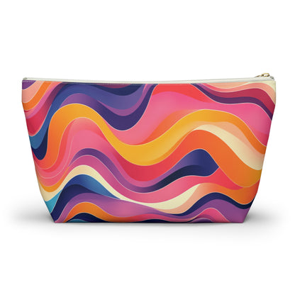 A zippered cosmetic travel bag with a colorful, wavy abstract pattern in shades of pink, orange, yellow, purple, and blue. The flowing curves evoke African-inspired patterns across the T-bottom pouch. The zipper is white with a gold-colored pull.