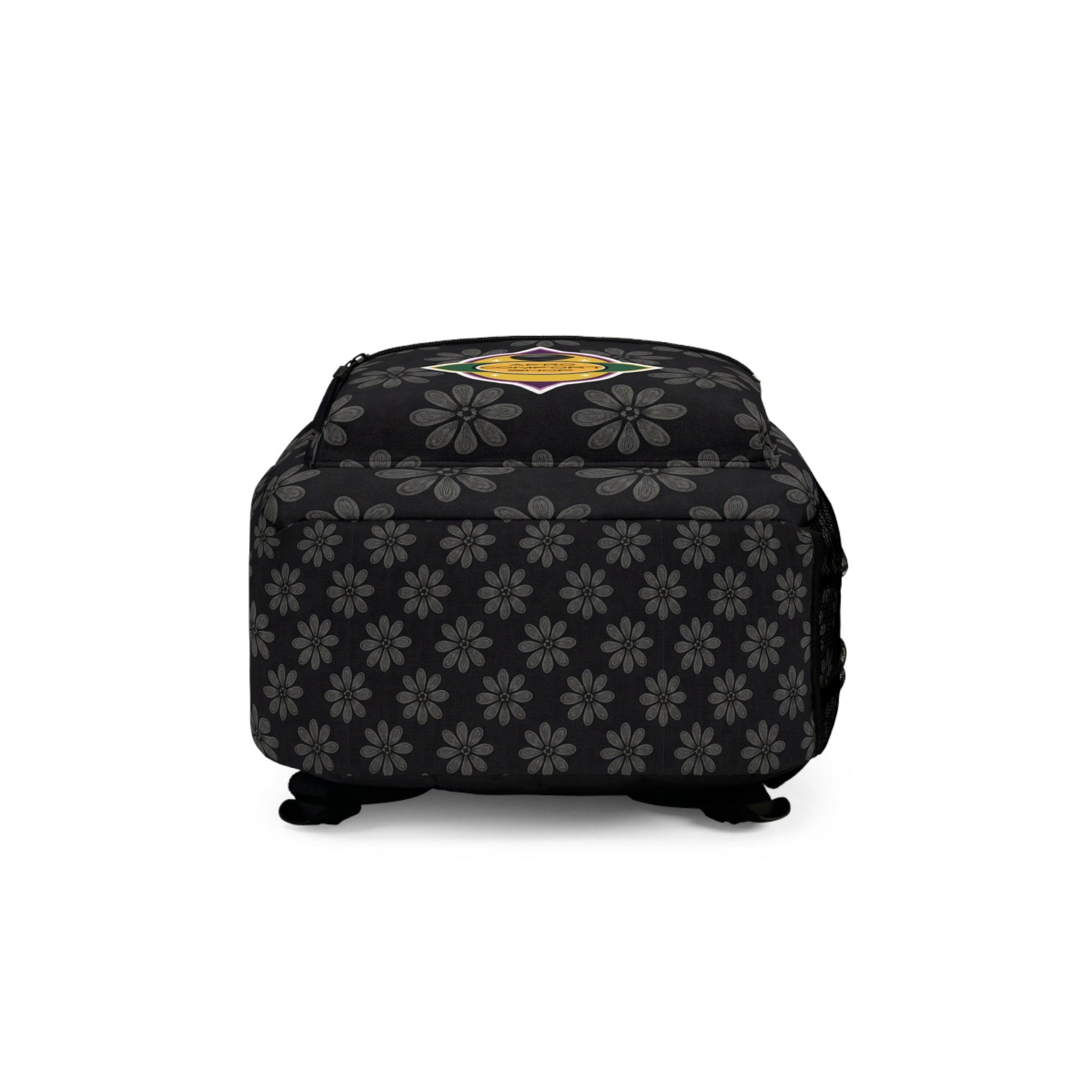 A square black ottoman with gray floral patterns and a colorful, round emblem featuring a yellow star on top, reminiscent of a stylish travel bag. The ottoman has short black feet, soft cushioning, and the floral motif wraps around its sides.