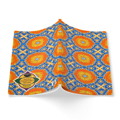 A colorful fabric is draped open, featuring a bold pattern of orange and yellow sunburst flowers with blue and white geometric shapes—perfect inspiration for an African-inspired journal. A yellow diamond-shaped label reads “AFRO COMFORT SHOE.” White background.