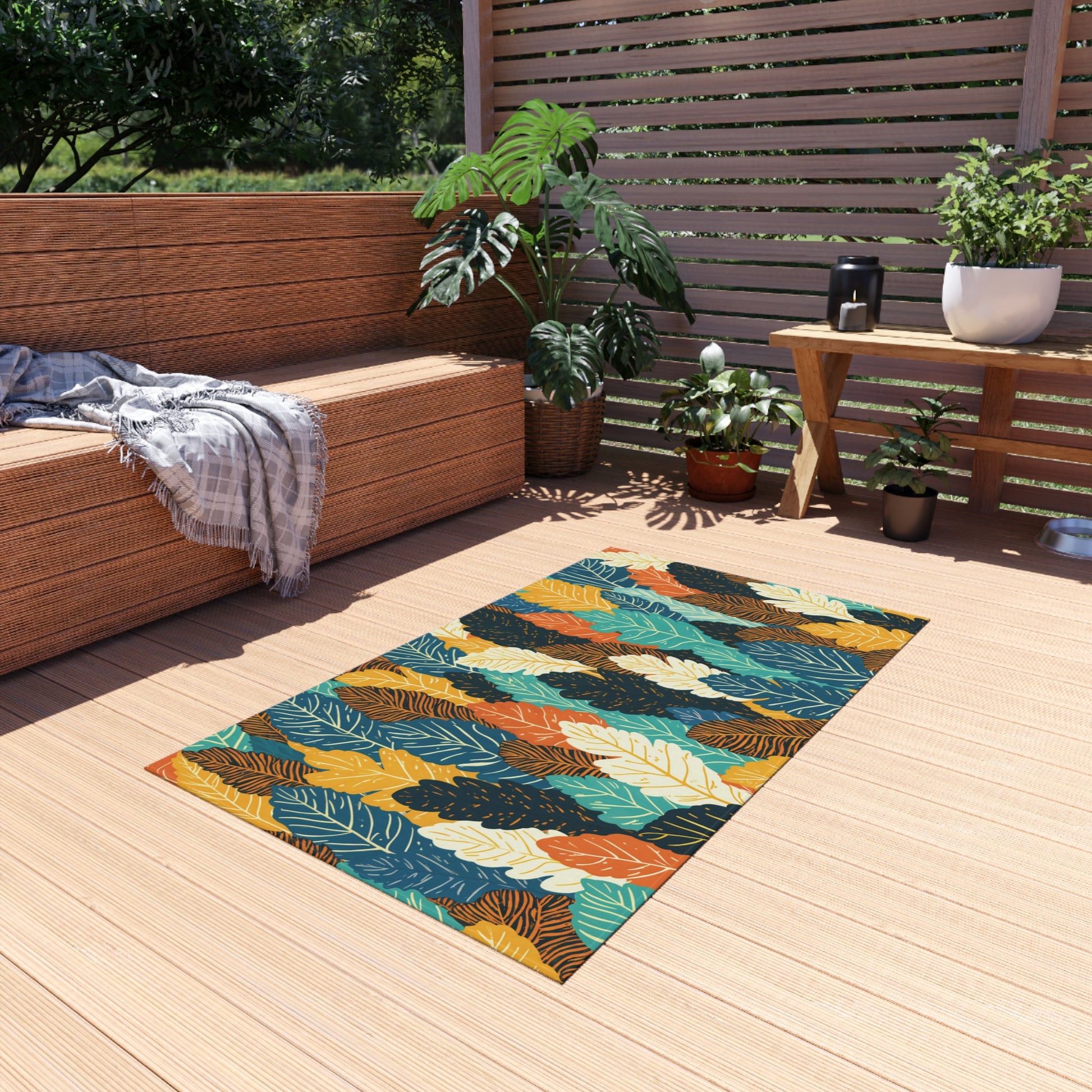 A colorful, African-inspired patterned rug with leaf designs lies on a light wood deck. Nearby, a modern wooden bench with a gray plaid blanket, potted plants, and a small black lantern create a cozy outdoor seating area surrounded by greenery.