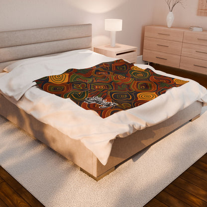 A neatly made bed in a modern, softly lit bedroom features an African-inspired personalized blanket with colorful swirls and geometric shapes laid across the foot. The word “Ebony” appears on this unique keepsake gift, complementing the light wood furniture and white rug.