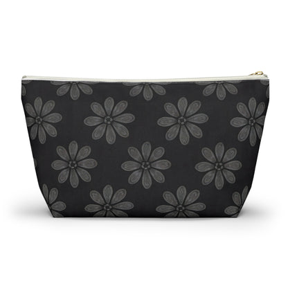 A zippered cosmetic travel bag with a black background, decorated with a repeating pattern of large, hand-drawn, gray daisy-like flowers. This T-bottom pouch tapers towards the base and features a white zipper and gold zipper pull.