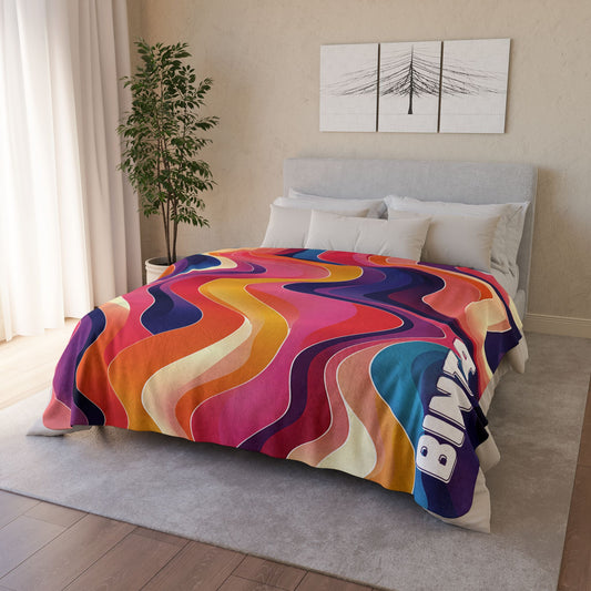 A modern bedroom with a bed covered by an African-inspired fleece blanket in vibrant wavy patterns and the word BING. There’s a potted plant, white curtains, and minimalist wall art above the bed for a cozy touch.