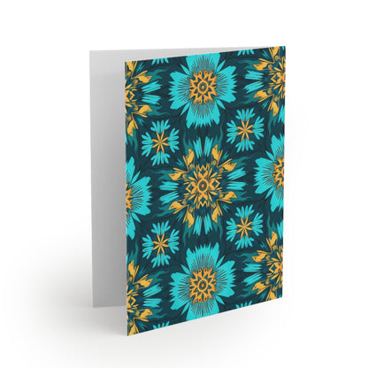 A greeting card stands open with a vibrant floral pattern on the front, inspired by African-inspired greeting cards. Blue and teal flowers with yellow and orange centers stand out against a dark background; the inside is blank and white.