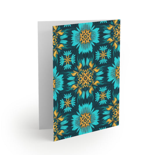 A greeting card stands open with a vibrant floral pattern on the front, inspired by African-inspired greeting cards. Blue and teal flowers with yellow and orange centers stand out against a dark background; the inside is blank and white.