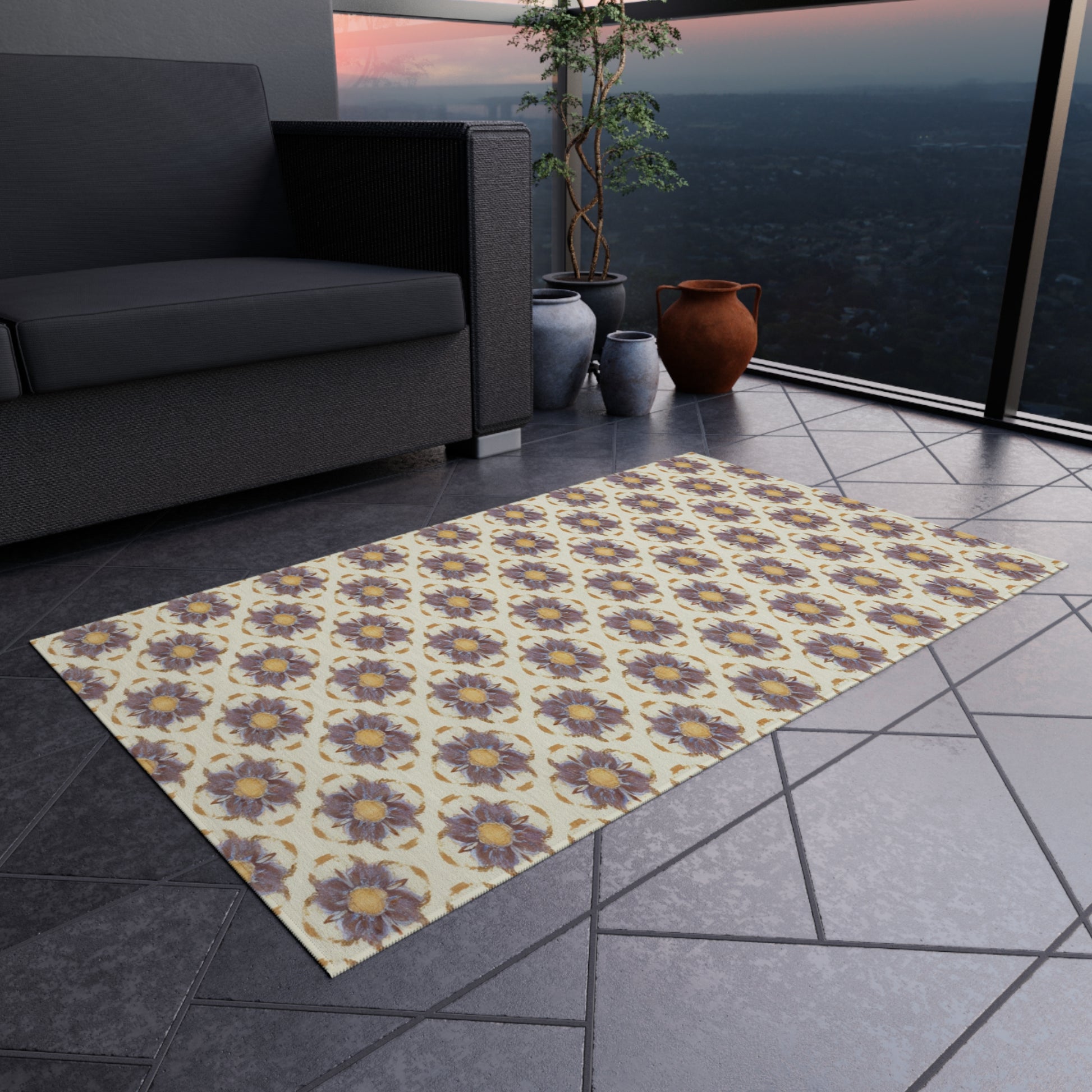 An African-inspired patterned rug with purple and yellow flowers lies on a gray tiled floor of a modern balcony. There’s a dark outdoor sofa, large potted plant, and terracotta jug. Glass railings offer sunset views of a distant cityscape.