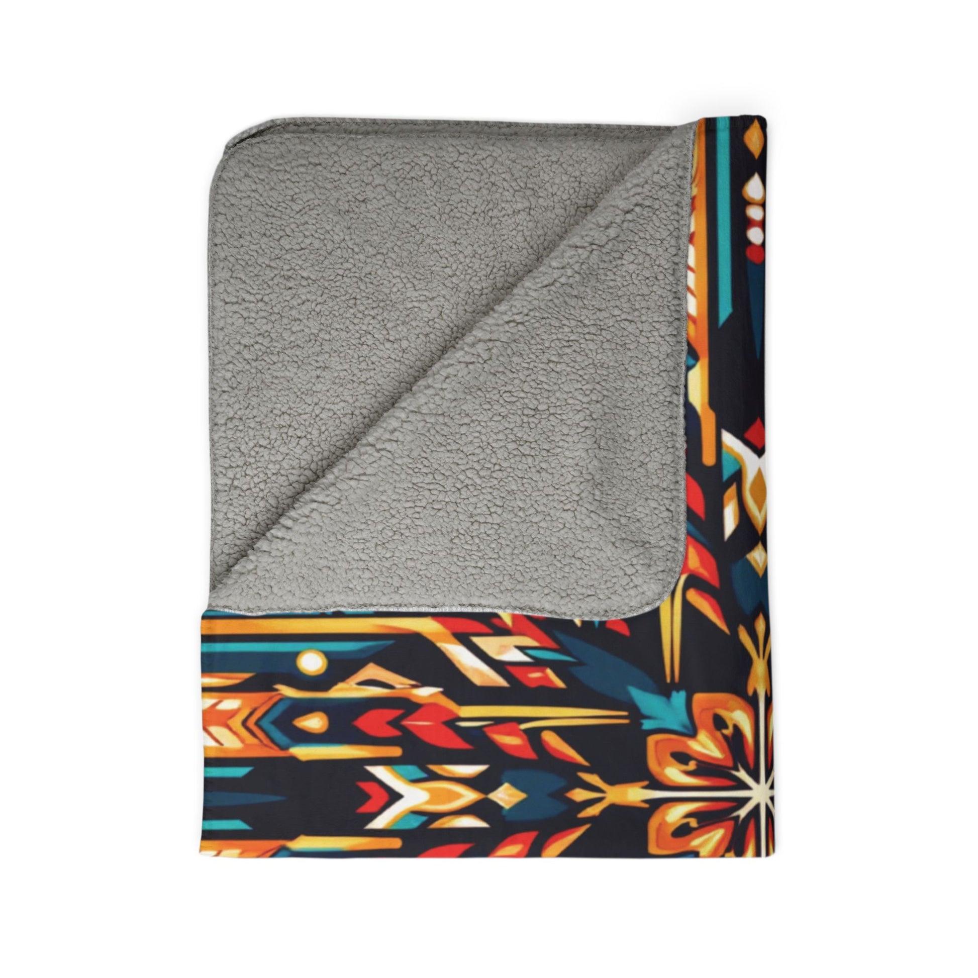 A folded blanket with a soft, light gray sherpa lining and an African-inspired geometric pattern on the outer side, featuring red, yellow, orange, teal, and white shapes on a black background. The vibrant pattern is visible along the border and corner.