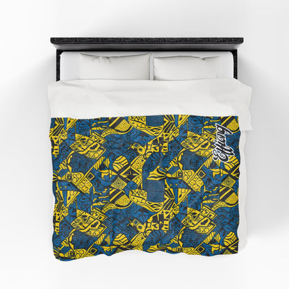 Overhead view of a bed with white pillows and a personalized velveteen blanket featuring a vibrant blue and yellow geometric and abstract pattern. Overlapping shapes, lines, and “Respect” in white script highlight this unique custom gift.