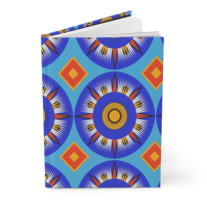 A hardcover journal with a blue cover featuring bold, geometric patterns of concentric circles in blue, white, and orange resembling starbursts, and orange diamonds. This vibrant, symmetrical African-inspired notebook is perfect as a lined writing journal.