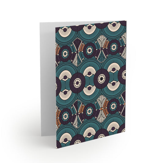 A greeting card stands upright, featuring an intricate pattern of overlapping teal, cream, and brown circular and geometric shapes with fine lines and dots—a beautiful example of premium stationery with a culturally inspired design. The background is white.