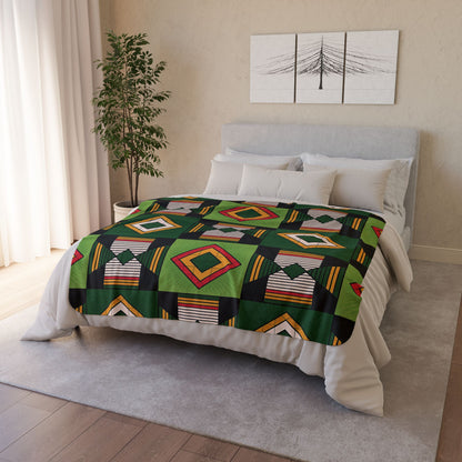 A neatly made bed showcases an African-inspired fleece blanket with vibrant geometric patterns in green, black, yellow, red, and white. The cozy home decor features a gray upholstered headboard, white bedding, a potted plant, and minimalist wall art.