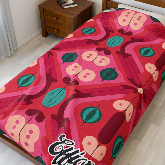 A single bed with a vibrant, African-inspired blanket in red, pink, and green hues, featuring abstract fruit and leaf shapes. The corner of the duvet has “Effort” in bold, cursive white letters. A wooden nightstand sits beside the bed.