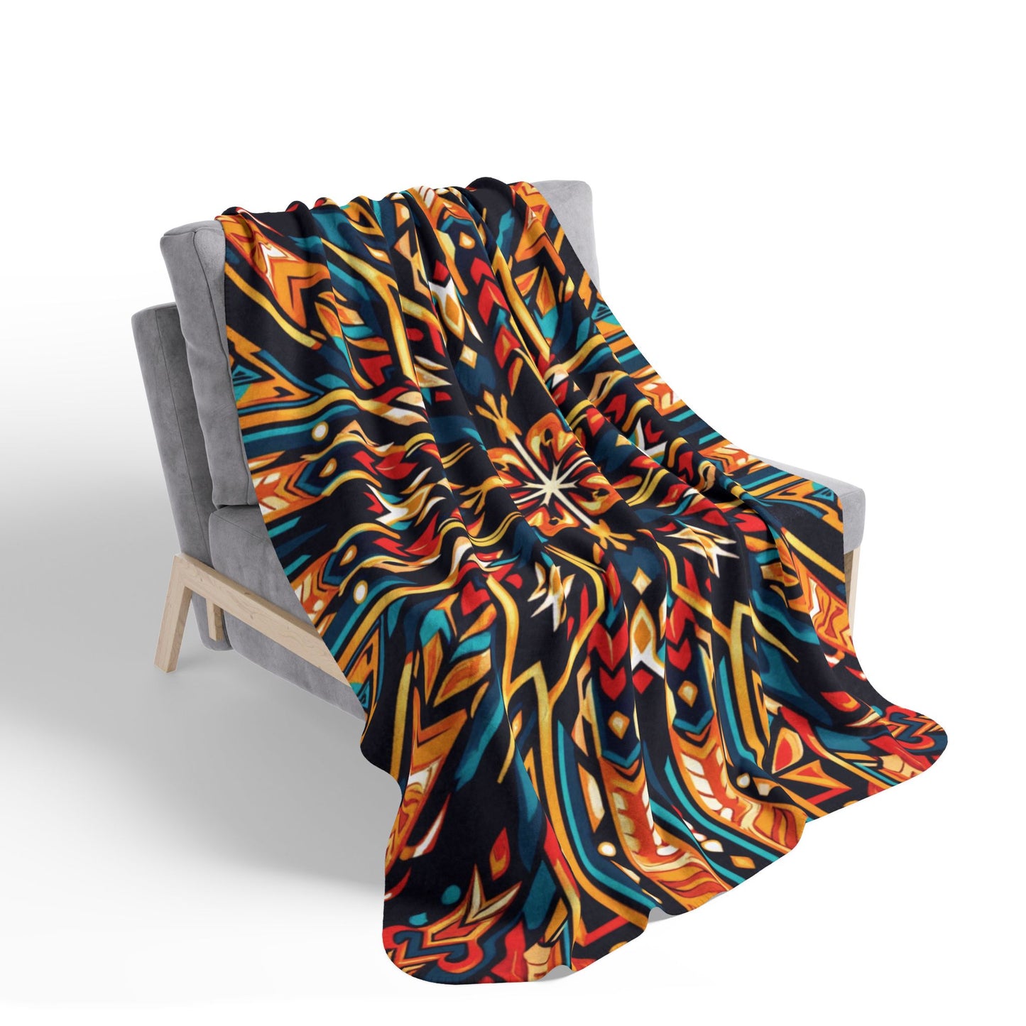 A soft grey chair draped with an African-inspired fleece blanket featuring an intricate geometric pattern in vibrant colors—yellow, orange, red, teal, and white—set against a black background. The setting is minimal, with a white backdrop.