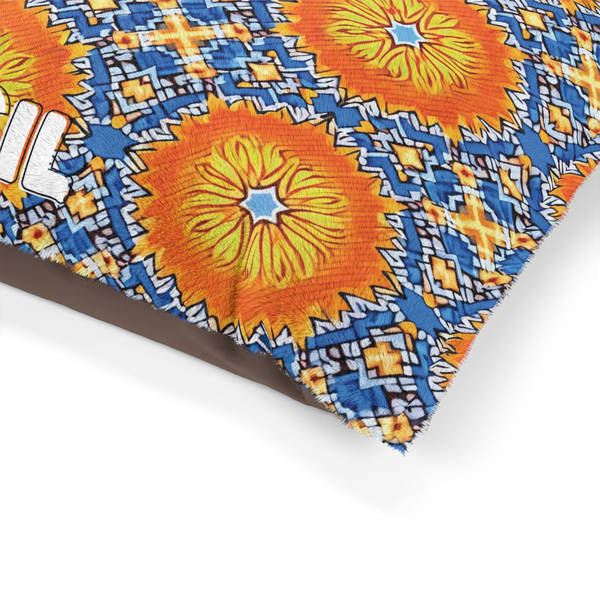 A close-up of a fabric for a stylish pet bed with a vibrant, geometric pattern featuring large orange and yellow sunburst shapes, blue and white diamond motifs, and black accents. The edge is slightly frayed with part of a white printed letter on the left.